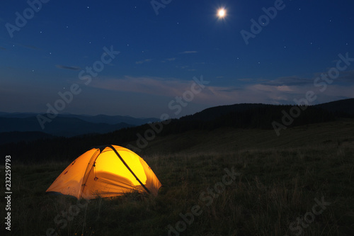 Illuminated orange tent at top of mountain at night