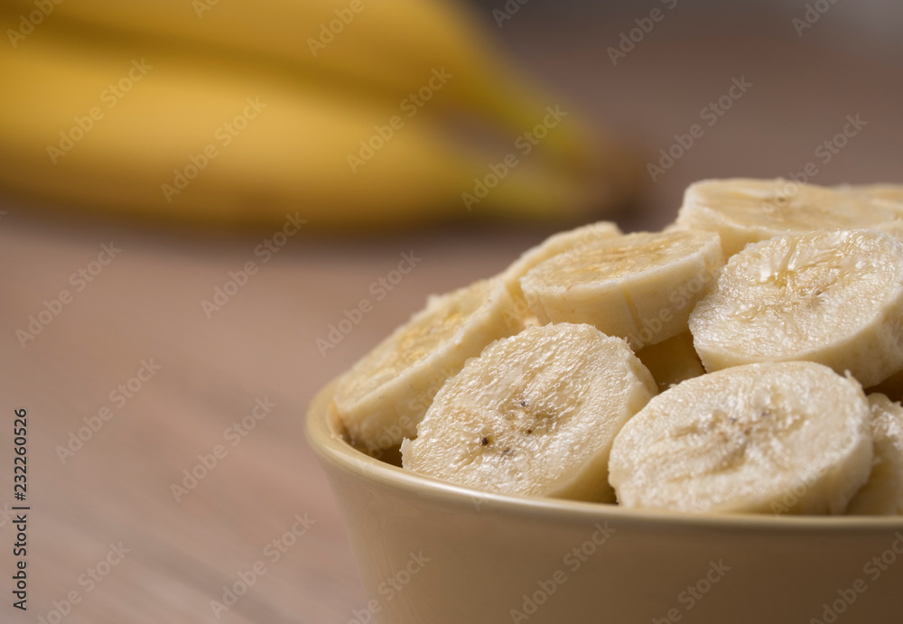 Sliced banana in ceramic bowl on wooden background. Close up.