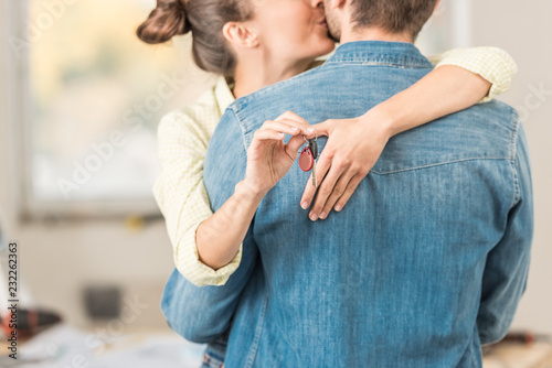 cropped shot of happy young woman hugging and kissing husband while holding key from new apartment
