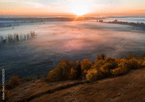 autumn atmosphere. Colorful trees in the foreground. Cold mist in the valley. The beauty of nature at sunrise.