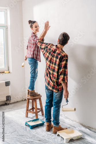 Fototapeta Naklejka Na Ścianę i Meble -  high angle view of young couple giving high five while painting wall in new apartment