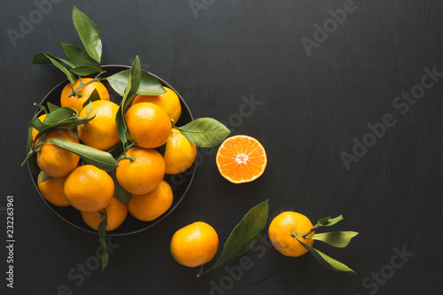 Fresh mandarins with leaves in bowl on black. Healthy eating concept. Copy space.