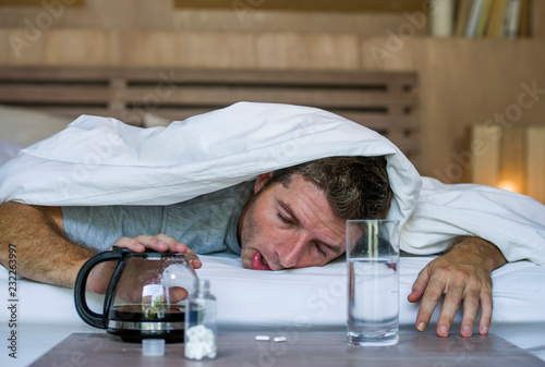 lifestyle home portrait of young exhausted and wasted man waking up suffering headache and hangover after drinking alcohol at night party lying on bed sick photo