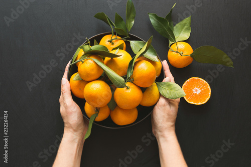 Fresh mandarins with leaves in female hand on black. Healthy eating concept. Copy space.
