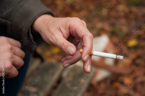closeup of man with cigarette in hand on wooden bench in outdoor