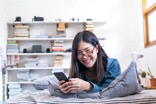 Slika na platnu Pretty asian woman with glasses lying on the bed reading good news on line in a