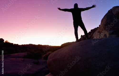 a person standing in a rocky landscape during sunset with stars in the sky