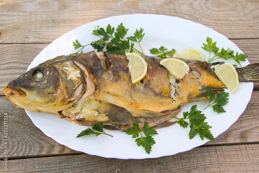 Tasty baked carp in white plate on wooden table. Top view