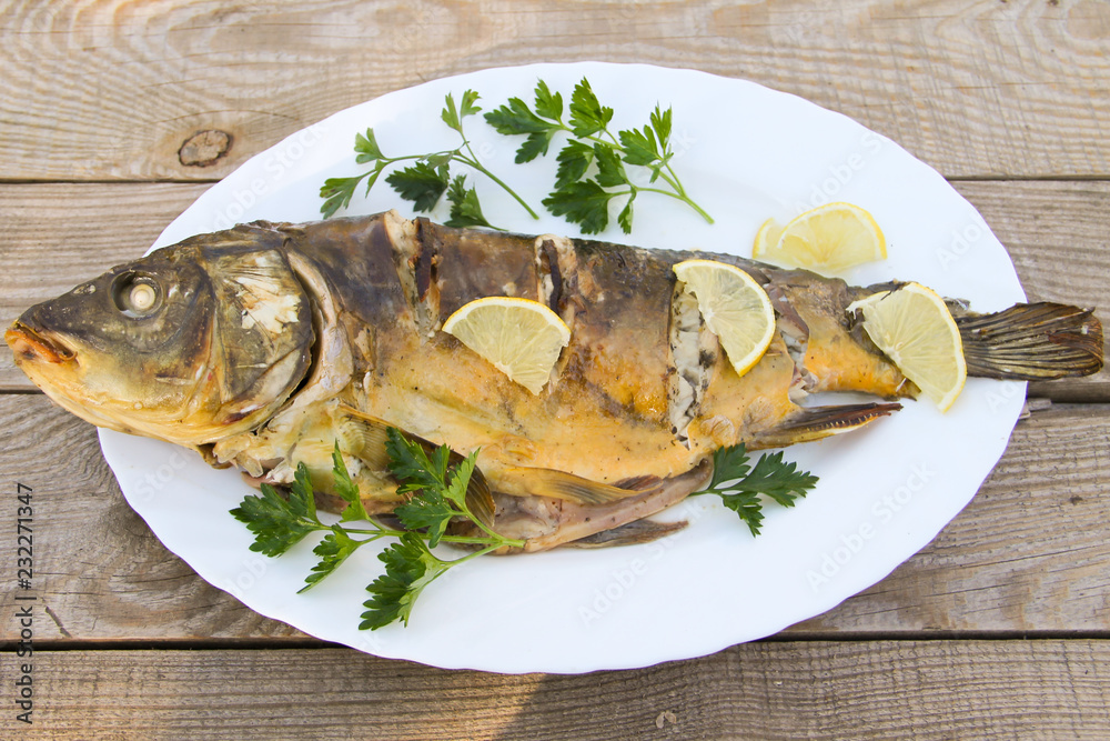 Tasty baked carp in white plate on wooden table. Top view Tasty baked carp in white plate on wooden table. Top view