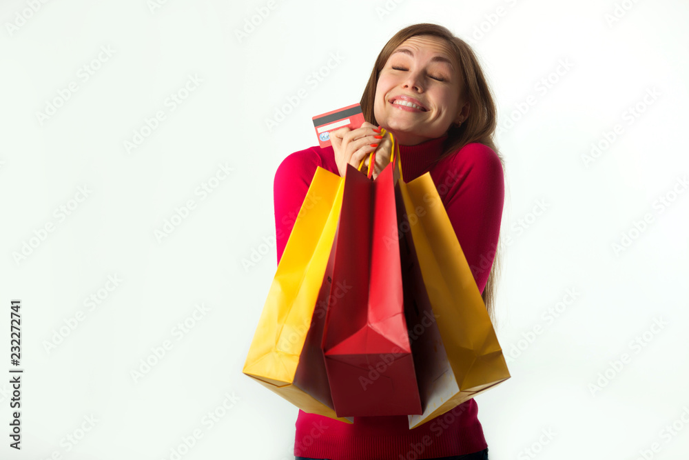beautiful young girl holding a purchase in soft bags on a white background with a payment card in her hand