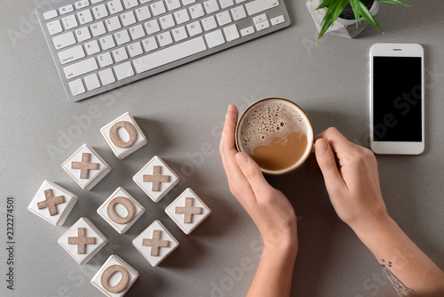 Woman drinking coffee at table with computer keyboard and tic tac toe cubes, top view photo