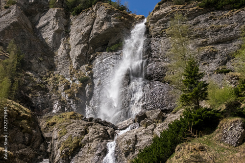spring mountain waterfall  with green vegetation and snow on a blue sky  