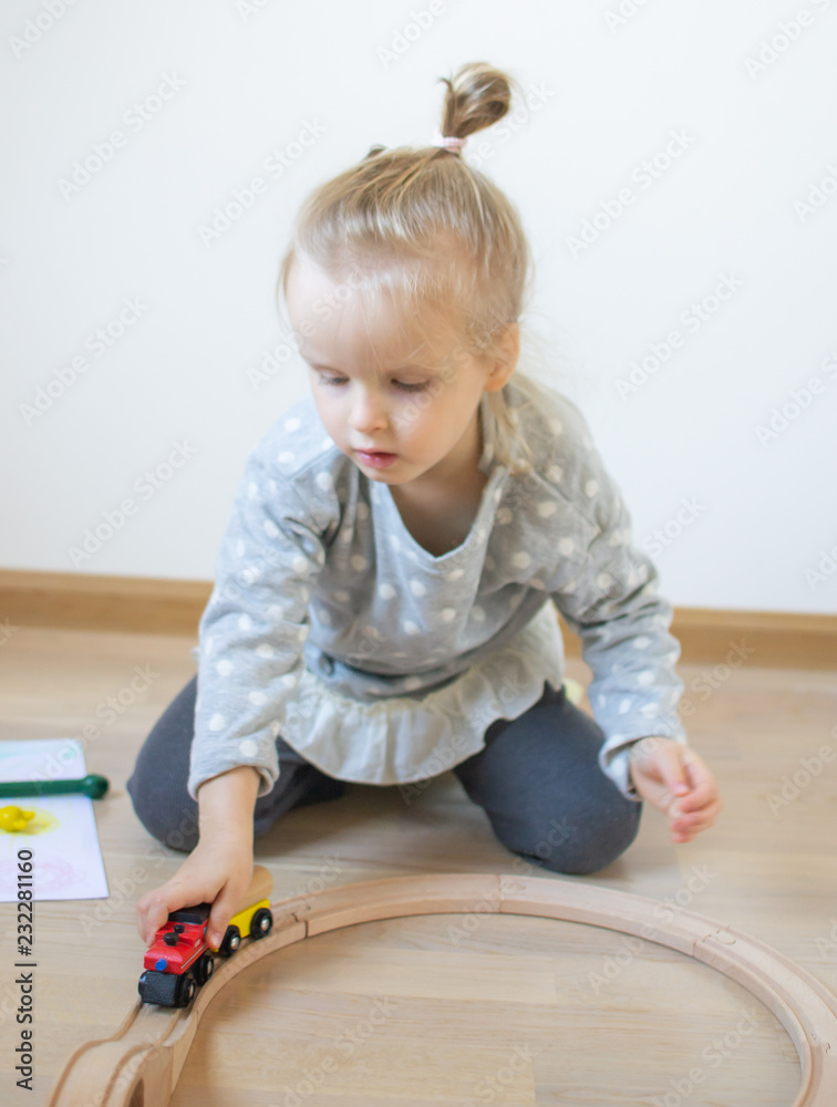 Naklejka premium Little Caucasian Girl Playing with Wooden Railway at Home Early Education Games Funny Development
