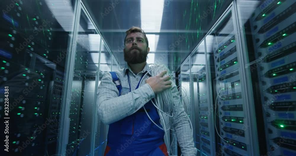 Medium shot of a male technician working in a data center carrying ...