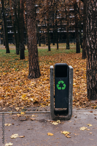 selective focus of trash bin with recycling sign in autumnal park with yellow leaves