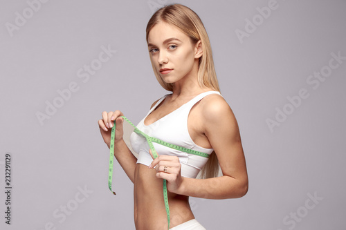 Portrait of beautiful young woman measuring her leg size with tape measure.