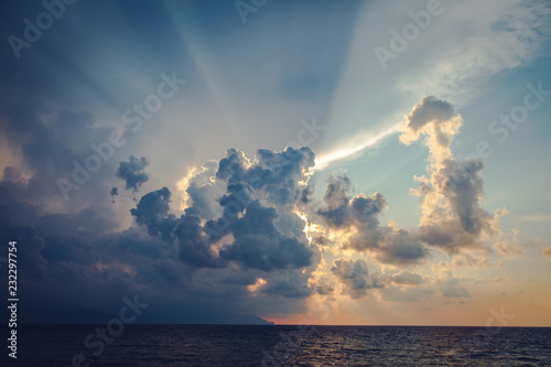 Sun rays and dark clouds on sky at the sea before sunset in the evening