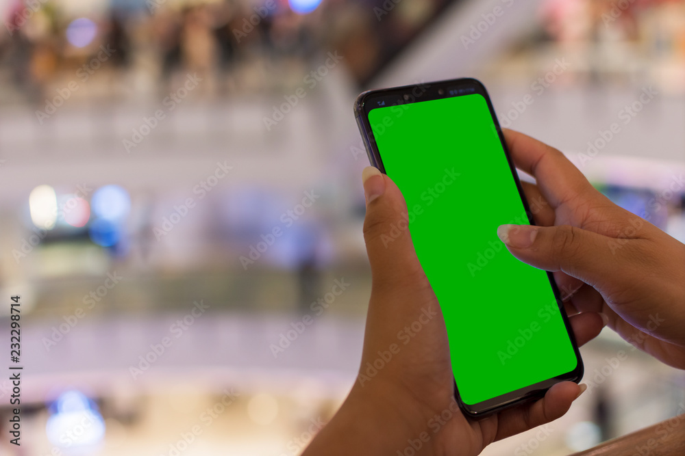 woman holding modern smartphone with green screen for replacement with blur background department store