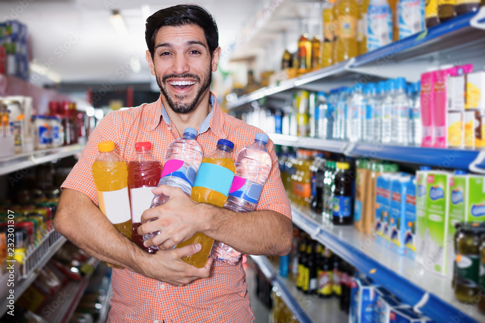 Positive male is posing with drinks in supermarket