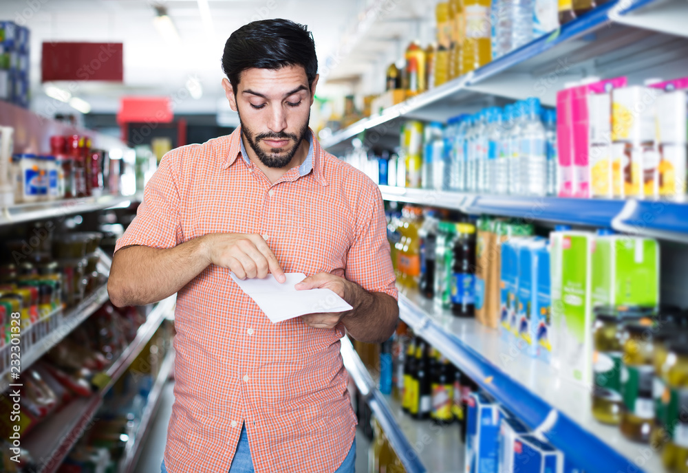Portrait of man customer who is standing with note list in supermarket.
