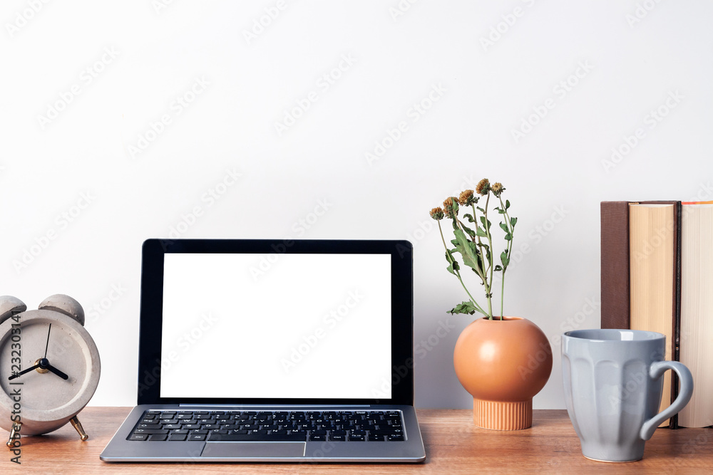Fototapeta premium Wooden desk with an open laptop mockup, a vase with dried flowers, a concrete gray clock, a mug of coffee and books on the background of a white wall copy space