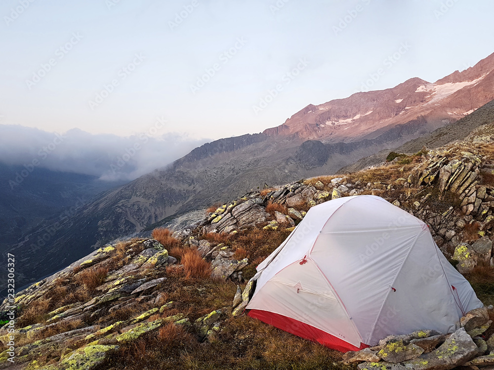 tent is illuminated at the top of the mountain, the waves of the misty sea float in the valley against the backdrop of high peaks covered in forests