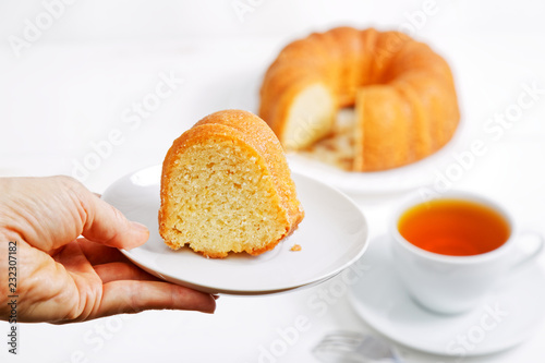 Closeup hand is holding a saucer with a piece of lemon cake. Homemade pie and cup of tea on a blurred background. Shallow focus.