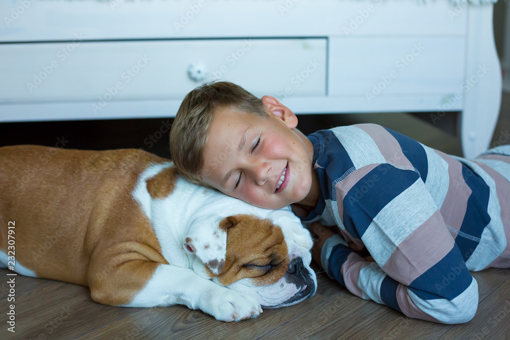 Handsome Young Boy kid wearing cozy pajamas Playing with His english funny bull Dog on the floor and enjoy life time weekend hanging each other with love and tender Handsome Young Boy kid wearing cozy pajamas Playing with His english funny bull Dog on the floor and enjoy life time weekend hanging each other with love and tender