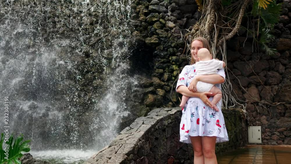 mother with child smiles and embracing baby son about waterfall kissing and talking with him. The concept of a happy family mother with child smiles and embracing baby son about waterfall kissing and talking with him. The concept of a happy family