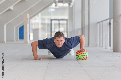 Young athletic man doing push ups with football ball photo