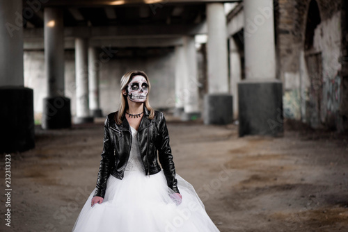 Portrait of zombie woman with painted skull face under a bridge.
