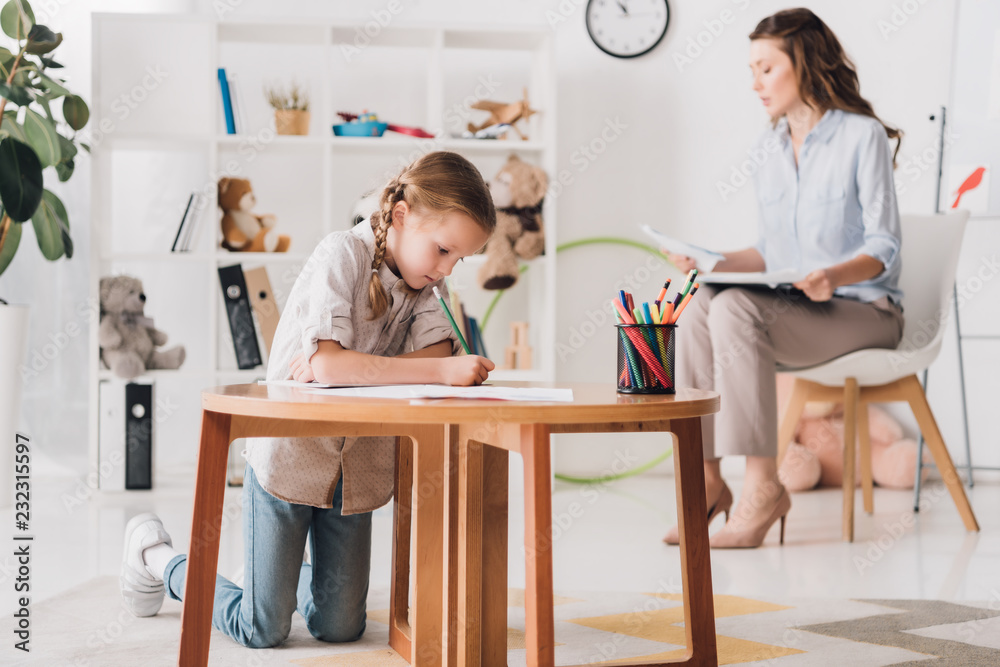 Obraz premium little child drawing while psychologist with clipboard sitting blurred on background