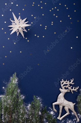 Фотография Christmas scene made of silver figurines of reindeer, star and evergreen branches on dark blue background