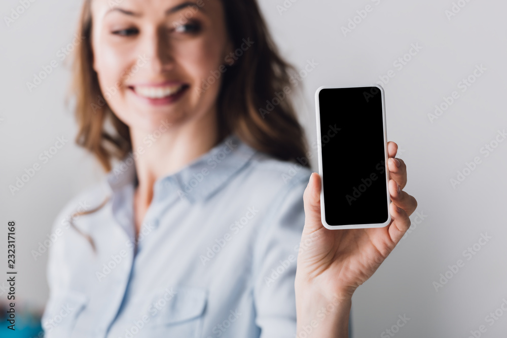 close-up portrait of happy adult woman in shirt showing smartphone with blank screen at camera