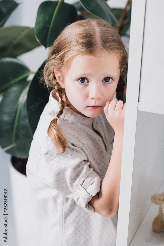 scared little child standing behind bookshelves and looking at camera scared little child standing behind bookshelves and looking at camera