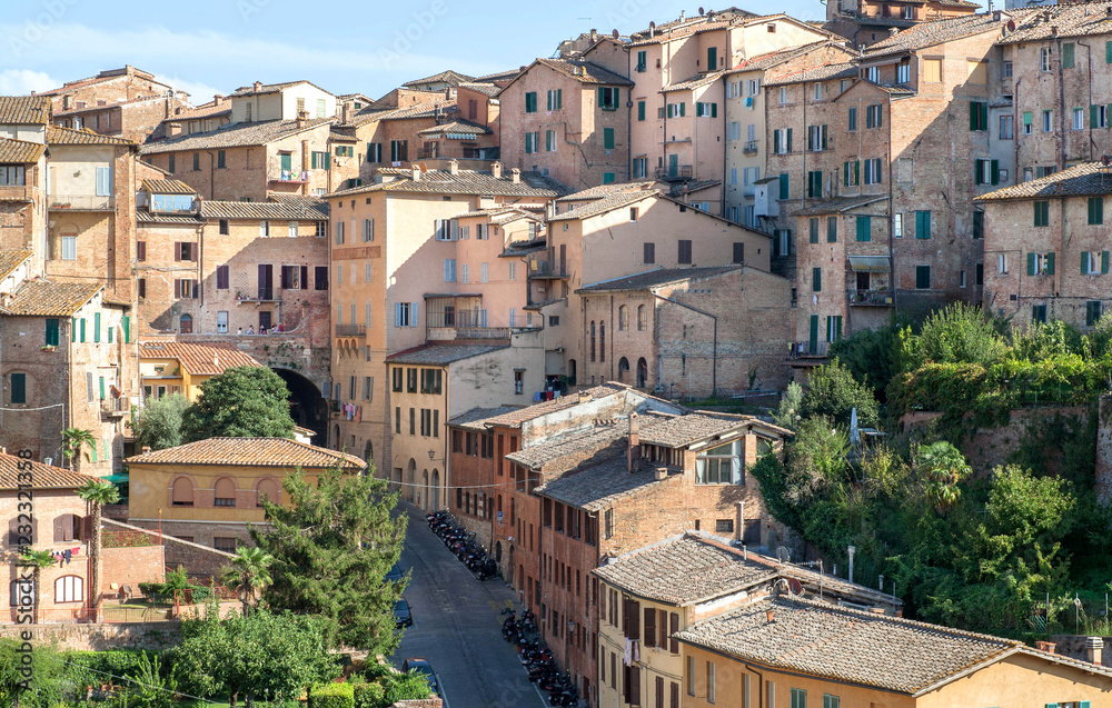 Shadows in Italian city with brick houses and towers of Siena, Tuscany. Tile roofs and brick structures in Italy