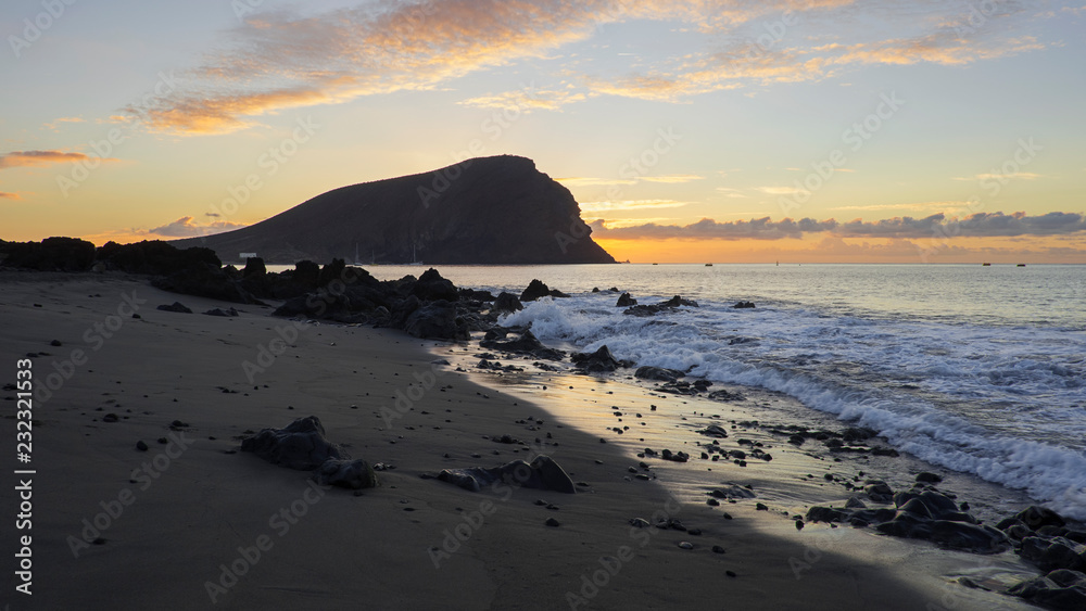 Dramatic sunrise over Montana Roja an unusual, stratovolcanic cone and La Tejita beach, one of the longest, natural beaches in Tenerife, Canary Islands, Spain. Panoramic perspective with natural light