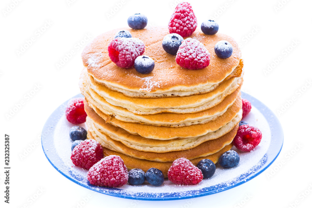 Pile of pancakes with blueberries and raspberries sprinkled with icing sugar