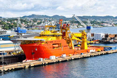 A large orange and yellow colored Offshore Construction Vessel (OCV) is in a dry dock of a shipyard and is being repaired