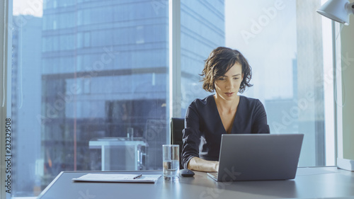 Beautiful Successful Businesswoman Working on a Laptop in Her Office with Cityscape View Window. Strong Independend Female CEO Runs Business Company. photo