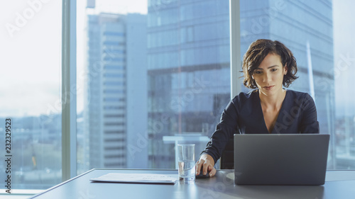 Beautiful Successful Businesswoman Working on a Laptop and Mouse in Her Office with Cityscape View Window. Strong Independend Female CEO Runs Business Company. photo