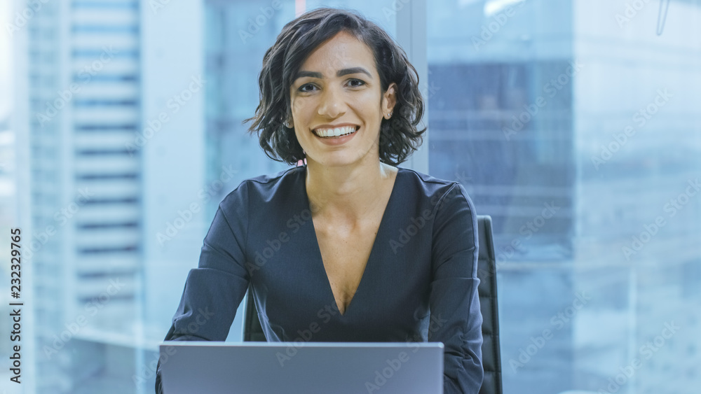 Portrait of the Successful Smiling Businesswoman Working on a Laptop in Her Office Looking at the Camera. Beautiful Independend Female CEO Runs Company.