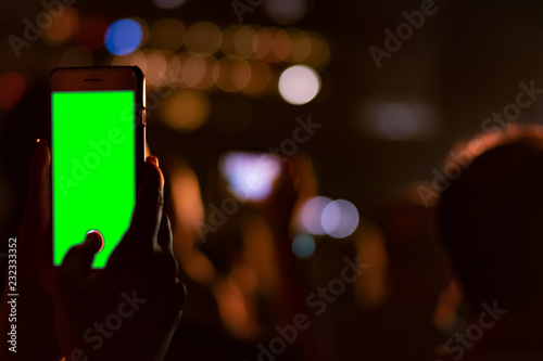 Two hands holding smartphone with a green screen in a vertical position at a concert