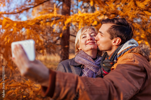 Middle-aged woman taking selfie with her adult son using phone. Family values