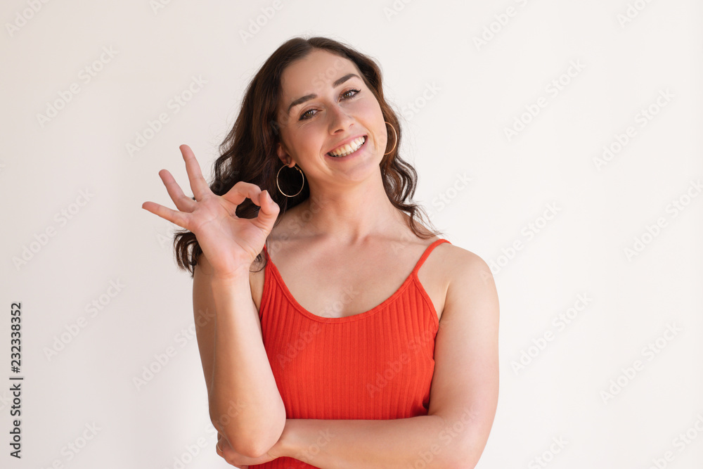 Positive pretty Caucasian girl making ok gesture with fingers and smiling. Young coach in red top satisfied with training results. Approval concept Positive pretty Caucasian girl making ok gesture with fingers and smiling. Young coach in red top satisfied with training results. Approval concept