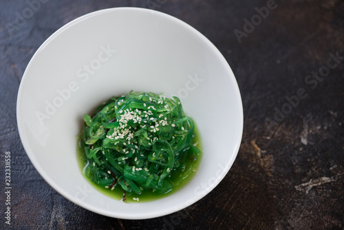 White bowl with seaweed salad on a dark brown stone background, horizontal shot with space