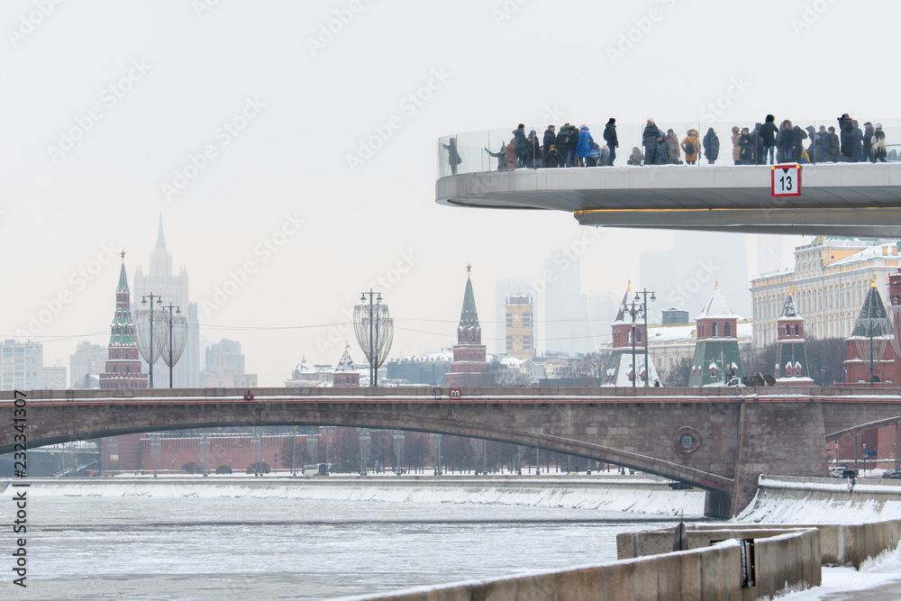 Observation deck with tourists on the background of the bridge over the frozen snow-covered river and the Kremlin tower.