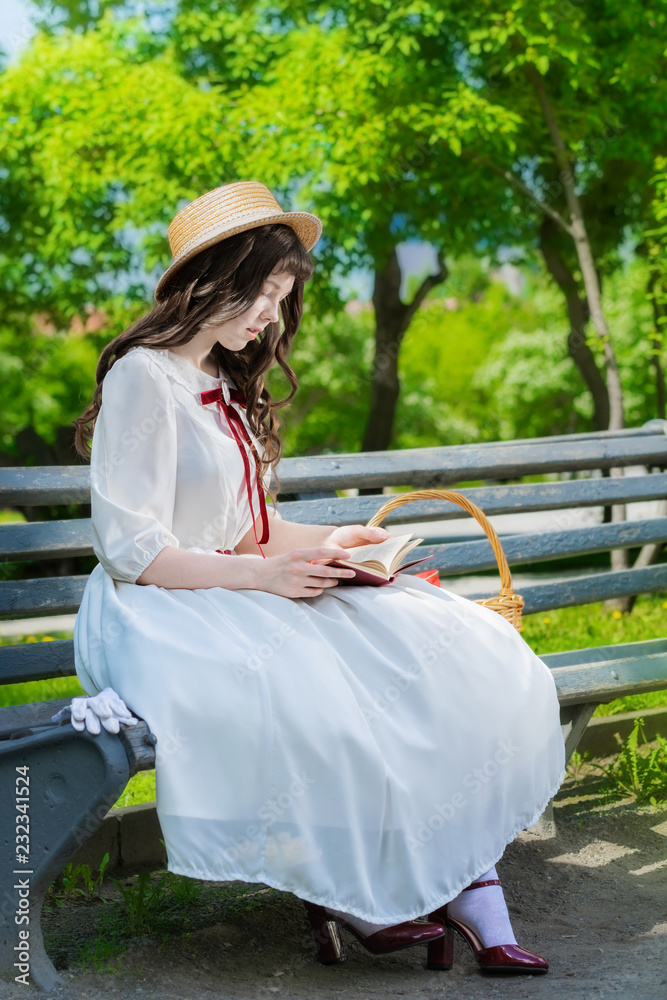 young girl is reading a book sitting on a bench.