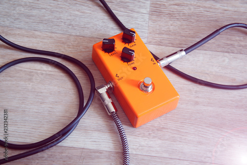 orange pedal effect and black cables on wooden floor. toning