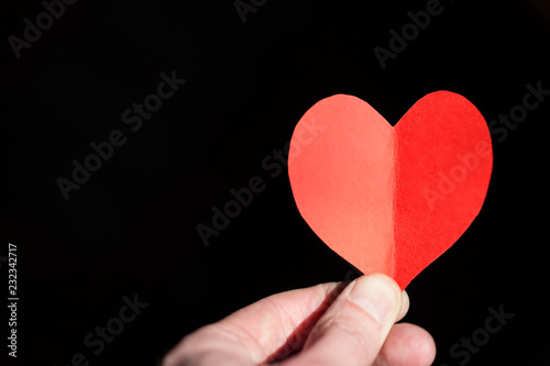 Red heart made from paper in the hand of a young man on a black background.